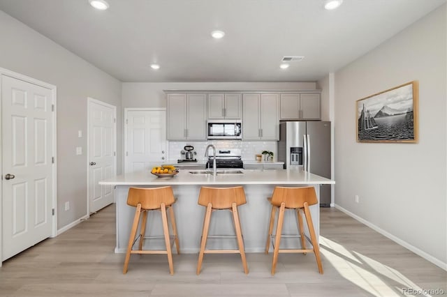 kitchen featuring appliances with stainless steel finishes, sink, a center island with sink, and gray cabinets