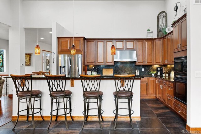 kitchen featuring range hood, decorative light fixtures, black appliances, a kitchen island with sink, and a breakfast bar