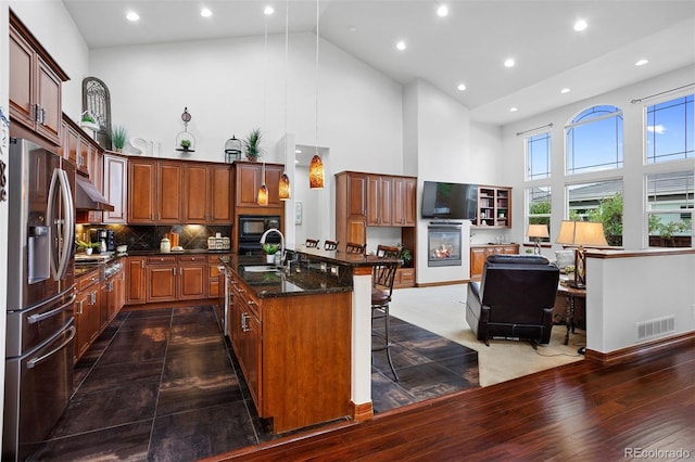 kitchen with exhaust hood, decorative light fixtures, a kitchen breakfast bar, appliances with stainless steel finishes, and high vaulted ceiling