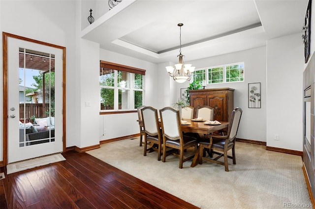 dining space featuring wood-type flooring, a wealth of natural light, a raised ceiling, and a notable chandelier