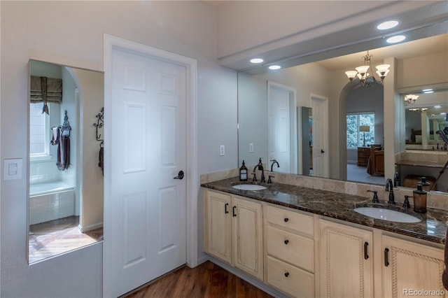 bathroom featuring hardwood / wood-style flooring, vanity, tiled tub, and a notable chandelier