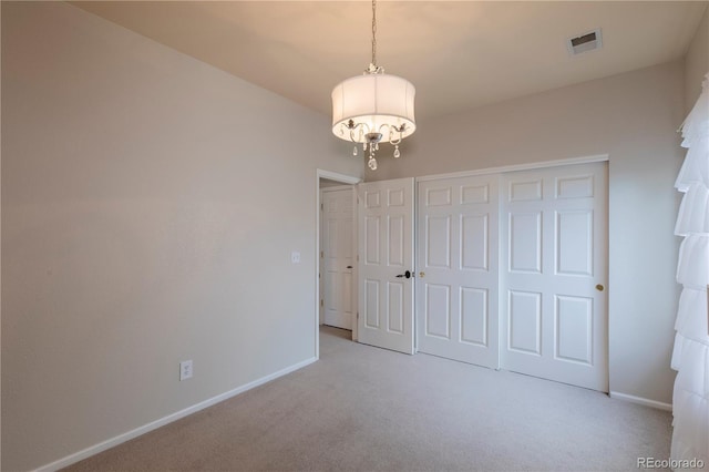 unfurnished bedroom featuring light carpet, an inviting chandelier, and a closet