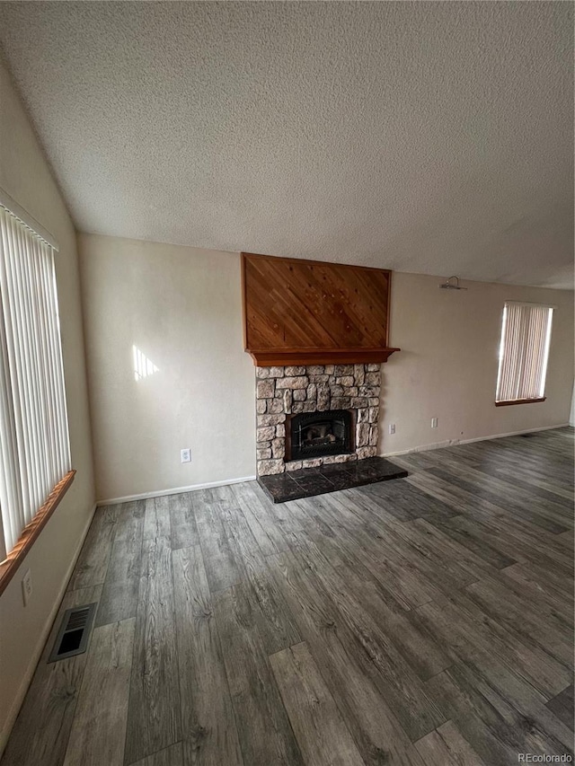 unfurnished living room featuring lofted ceiling, visible vents, a stone fireplace, a textured ceiling, and wood finished floors