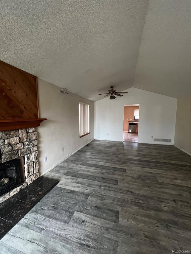 unfurnished living room with lofted ceiling, ceiling fan, wood finished floors, a textured ceiling, and a stone fireplace