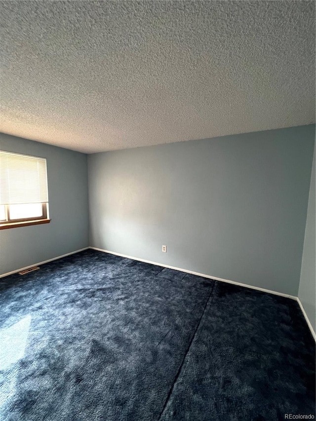 empty room featuring a textured ceiling, dark colored carpet, visible vents, and baseboards