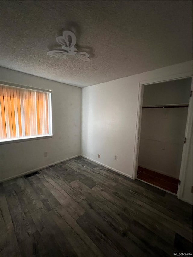 unfurnished bedroom with visible vents, a textured ceiling, baseboards, and wood finished floors