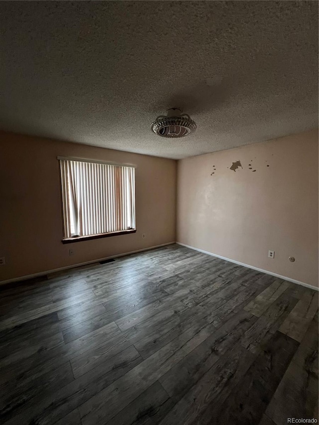 spare room with a textured ceiling, baseboards, and dark wood-style flooring