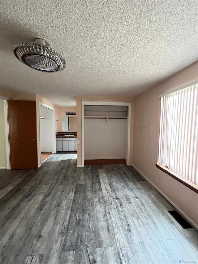 unfurnished living room with baseboards, a textured ceiling, visible vents, and wood finished floors