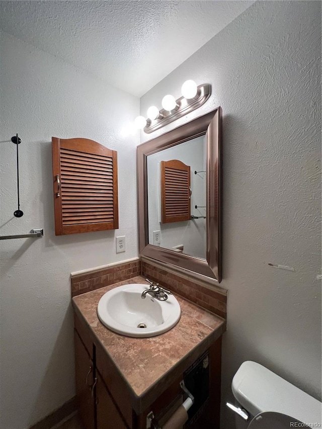 bathroom with a textured ceiling, a textured wall, toilet, vanity, and tasteful backsplash