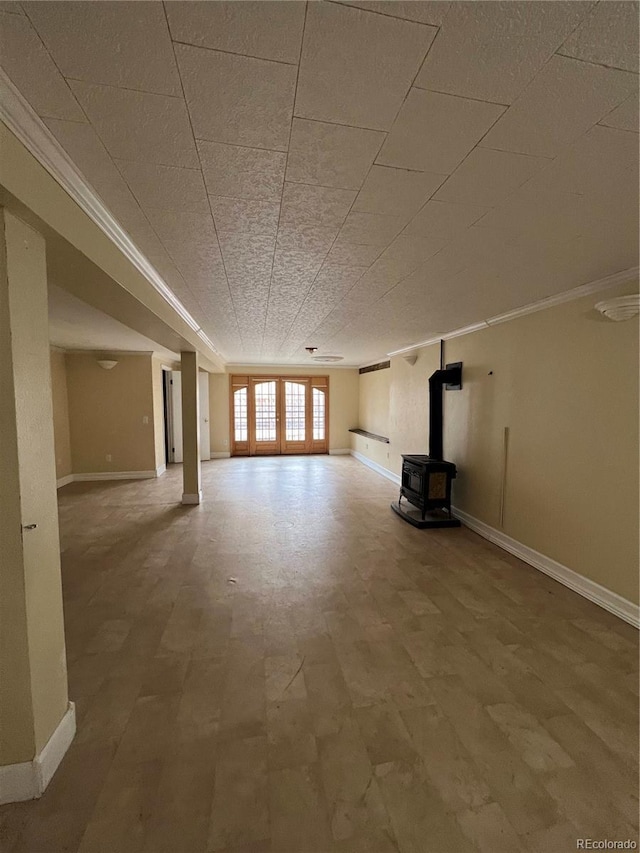 unfurnished living room featuring a wood stove, baseboards, ornamental molding, and french doors