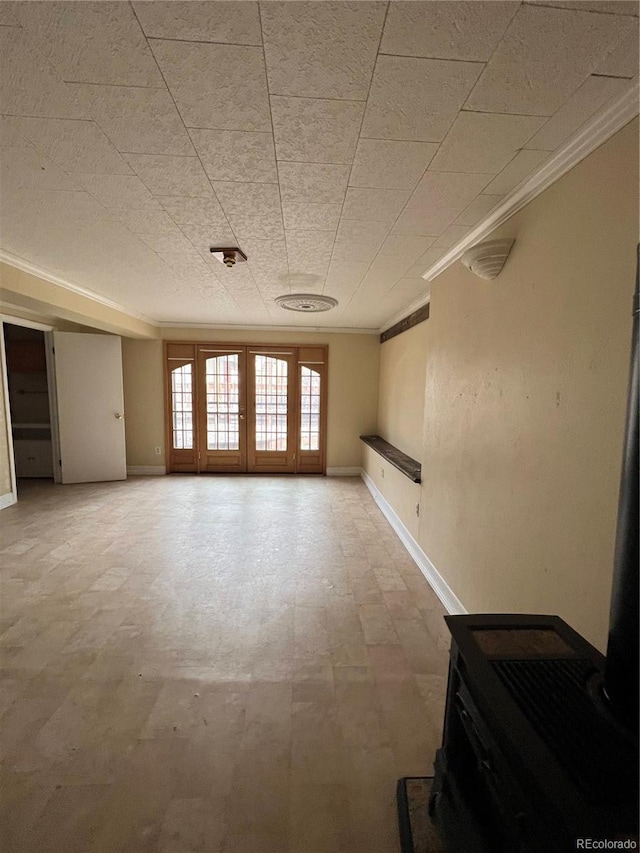 spare room featuring ornamental molding, french doors, baseboards, and a wood stove