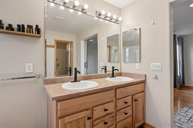 bathroom with wood finished floors, double vanity, a sink, and a textured wall