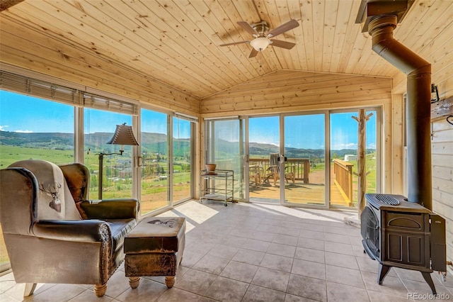 sunroom / solarium featuring ceiling fan, vaulted ceiling, a mountain view, a wood stove, and wooden ceiling