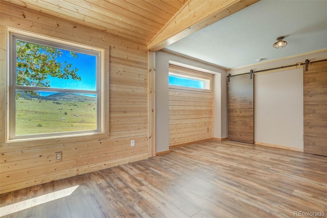 unfurnished bedroom with light wood-type flooring, wooden walls, a barn door, and vaulted ceiling