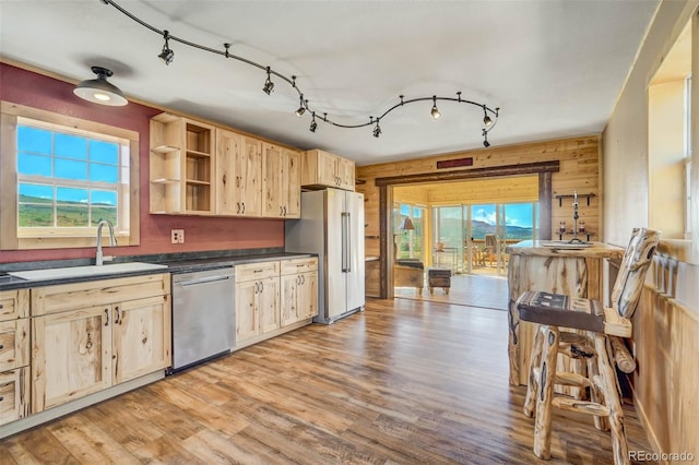 kitchen featuring appliances with stainless steel finishes, light brown cabinetry, sink, wood walls, and light wood-type flooring