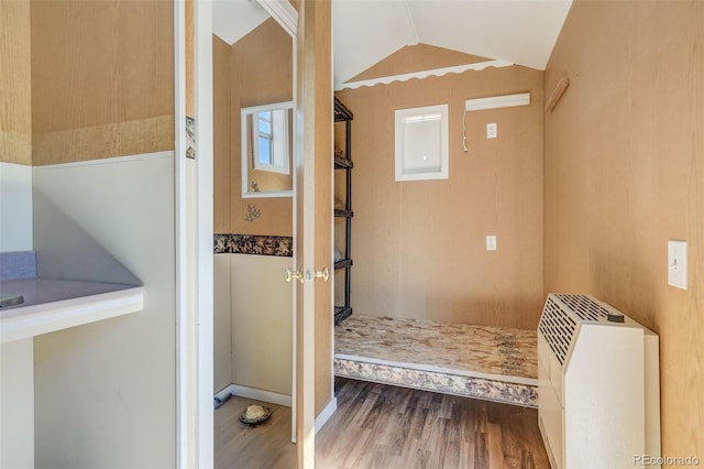 interior space with heating unit, vaulted ceiling, electric panel, and hardwood / wood-style floors