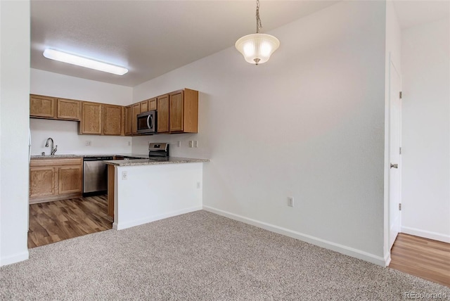 kitchen with appliances with stainless steel finishes, brown cabinets, decorative light fixtures, light countertops, and a sink