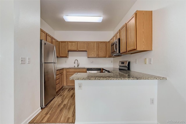 kitchen featuring stainless steel appliances, brown cabinetry, a sink, light wood-type flooring, and a peninsula