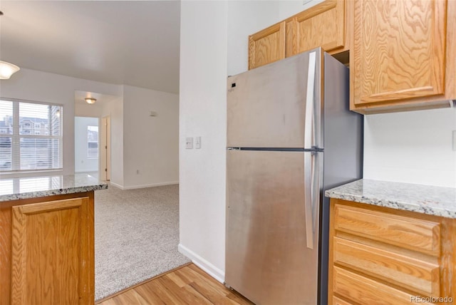 kitchen with light stone counters, light wood-style flooring, light colored carpet, baseboards, and freestanding refrigerator