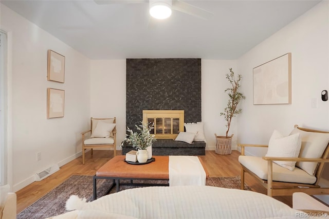 interior space featuring a ceiling fan, visible vents, a fireplace, and wood finished floors