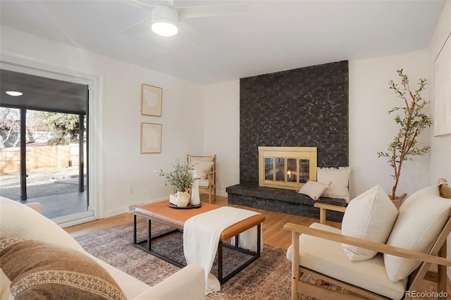 living area featuring ceiling fan, a fireplace, baseboards, and wood finished floors