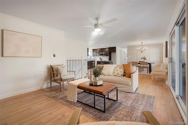 living area with light wood-style floors, baseboards, and ceiling fan with notable chandelier