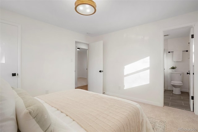 carpeted bedroom featuring ensuite bath and baseboards