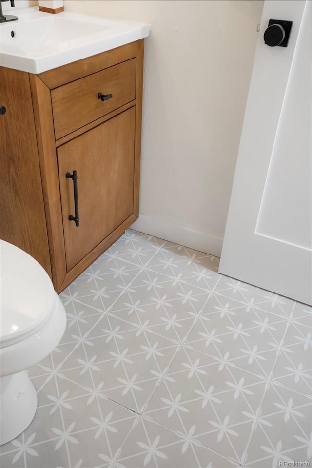 half bathroom featuring baseboards, vanity, toilet, and tile patterned floors