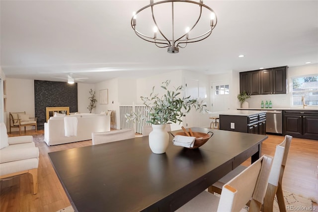 dining space featuring recessed lighting, a fireplace, light wood finished floors, and ceiling fan with notable chandelier