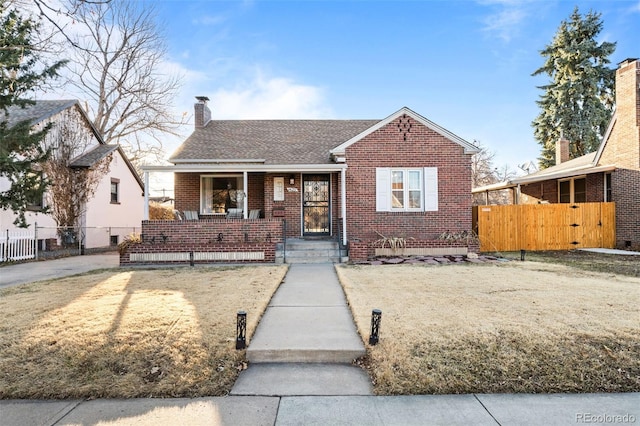 bungalow-style home with a shingled roof, a chimney, fence, a porch, and brick siding