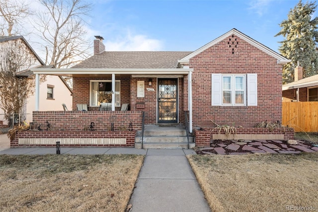 view of front facade with a porch, brick siding, fence, a chimney, and a front yard