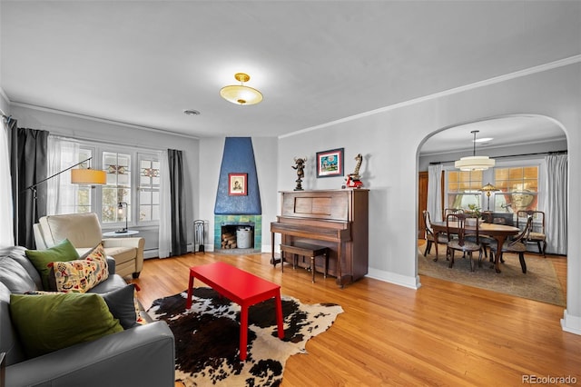 living room featuring light wood-type flooring, arched walkways, a fireplace, and ornamental molding