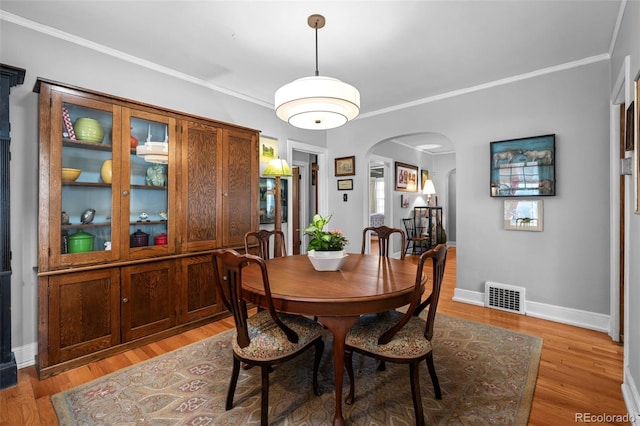 dining room featuring arched walkways, visible vents, crown molding, and light wood-style flooring