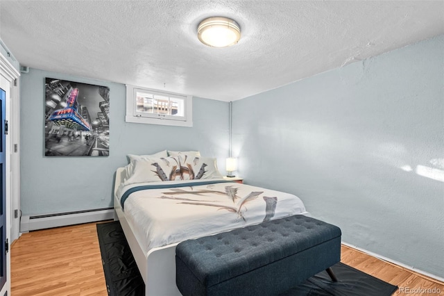 bedroom with a baseboard heating unit, light wood-type flooring, and a textured ceiling