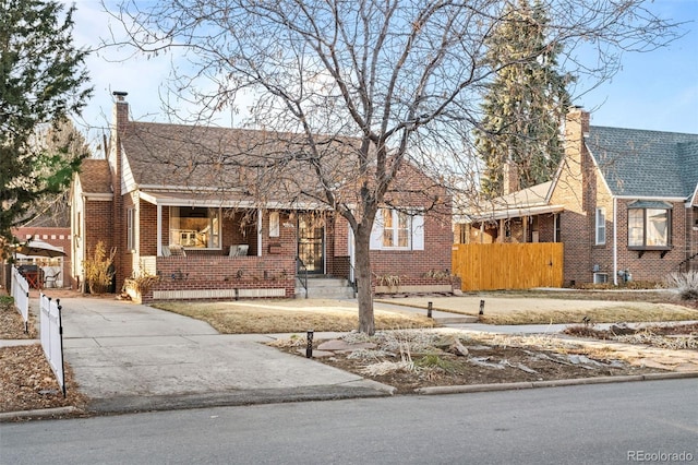 view of front of house with brick siding, fence, a chimney, and roof with shingles