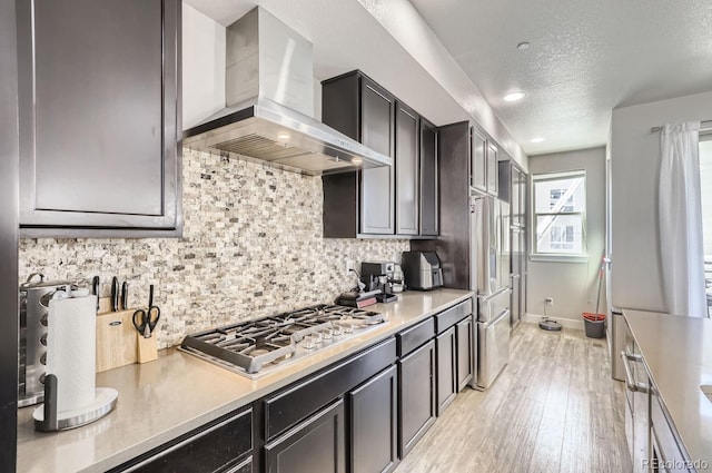 kitchen with light hardwood / wood-style floors, a textured ceiling, tasteful backsplash, stainless steel appliances, and wall chimney exhaust hood