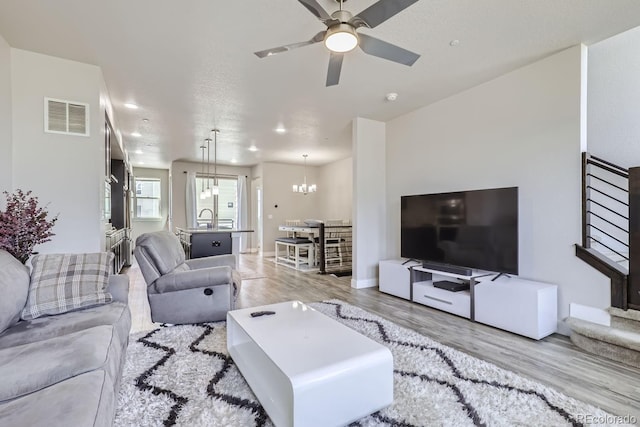 living room featuring sink, light hardwood / wood-style floors, and ceiling fan with notable chandelier