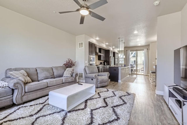 living room featuring sink, light wood-type flooring, a textured ceiling, and ceiling fan