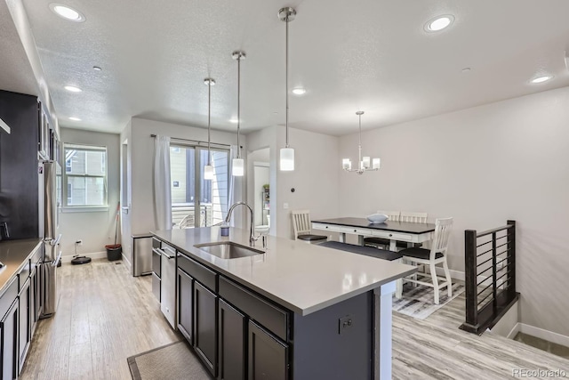 kitchen with stainless steel fridge, sink, decorative light fixtures, a kitchen island with sink, and a textured ceiling