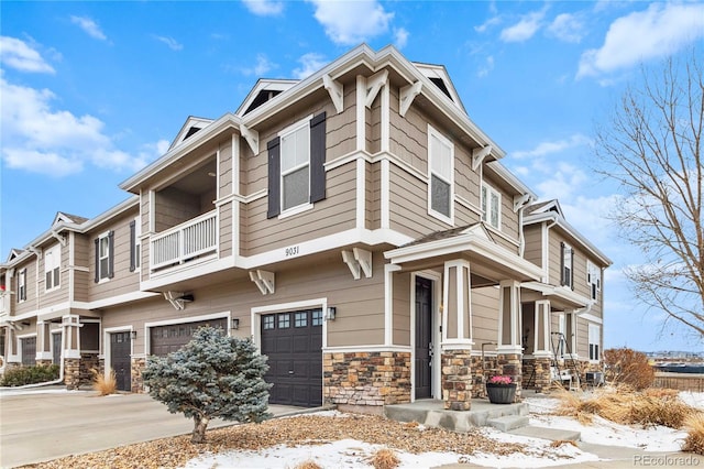 snow covered property with stone siding, an attached garage, and driveway