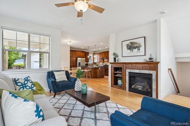 living room featuring a ceiling fan, a tiled fireplace, baseboards, light wood-style floors, and recessed lighting
