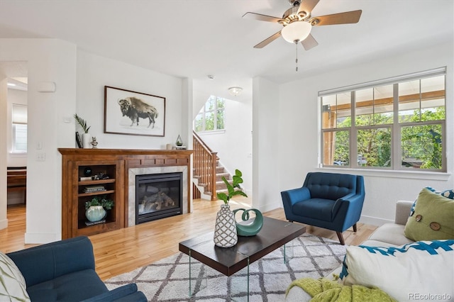 living area with baseboards, a fireplace, light wood-style flooring, and a ceiling fan