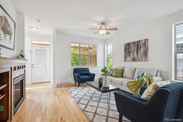 living room with light wood-type flooring, a wealth of natural light, a ceiling fan, and a glass covered fireplace