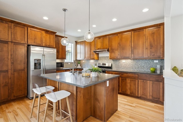 kitchen with brown cabinetry, light wood-style floors, appliances with stainless steel finishes, and under cabinet range hood