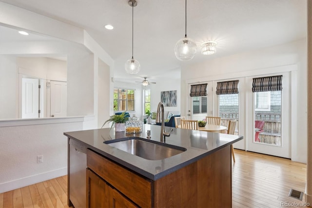 kitchen featuring stainless steel dishwasher, brown cabinetry, hanging light fixtures, a sink, and light wood-type flooring