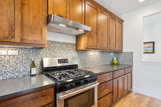 kitchen featuring brown cabinets, under cabinet range hood, gas range, dark countertops, and light wood-style floors