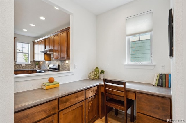 kitchen featuring under cabinet range hood, stainless steel range, decorative backsplash, and brown cabinetry