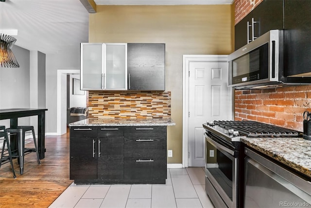 909 W Park Ave, Denver, CO 80205 - kitchen featuring stainless steel appliances, tasteful backsplash, light stone countertops, dark cabinetry, and light tile patterned floors