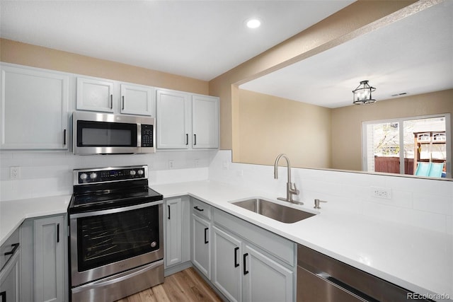 kitchen with light countertops, appliances with stainless steel finishes, a sink, and tasteful backsplash