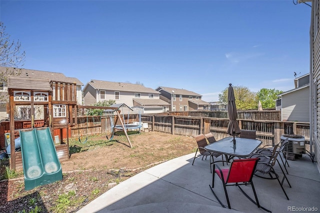 view of patio featuring a residential view, outdoor dining space, a fenced backyard, central AC unit, and a playground
